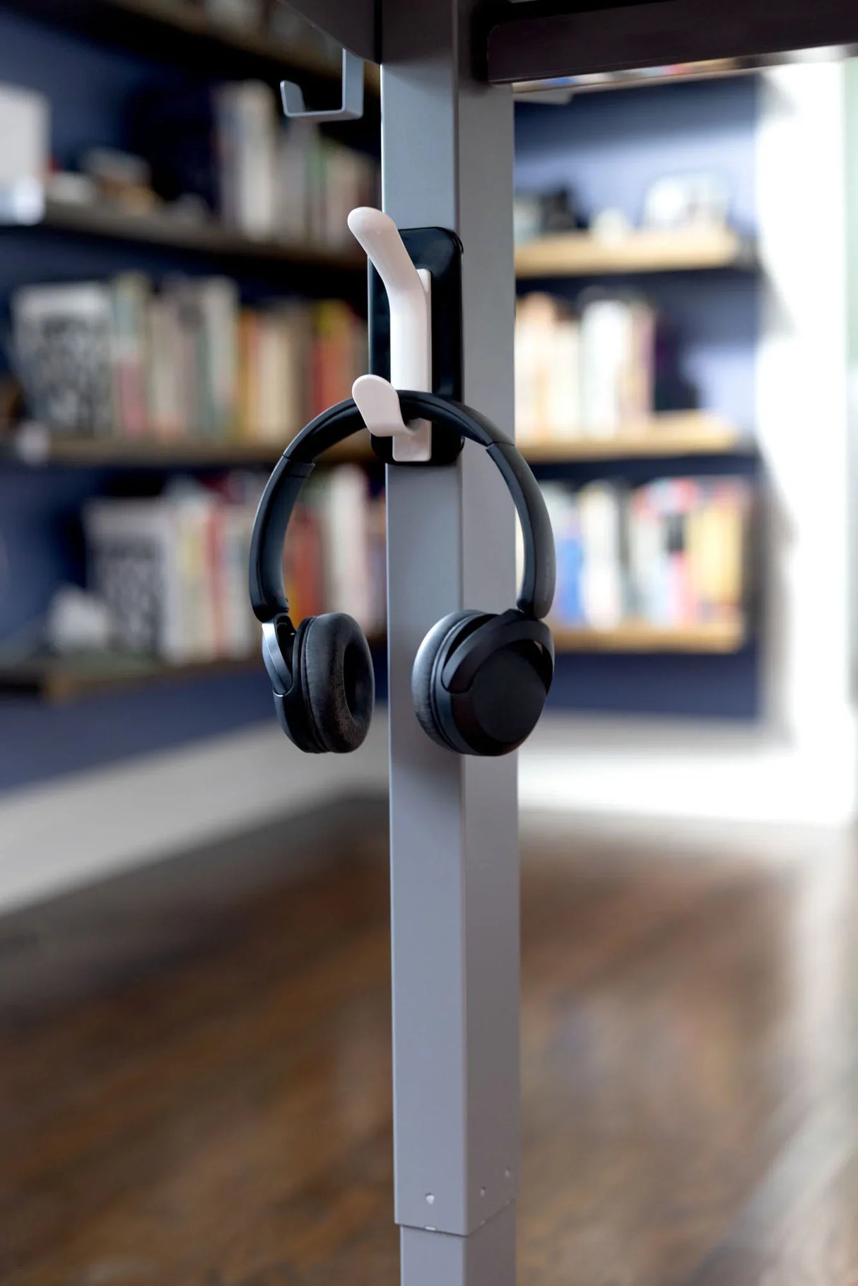 Black headphones on desk hook in organized office workspace with shelves in background