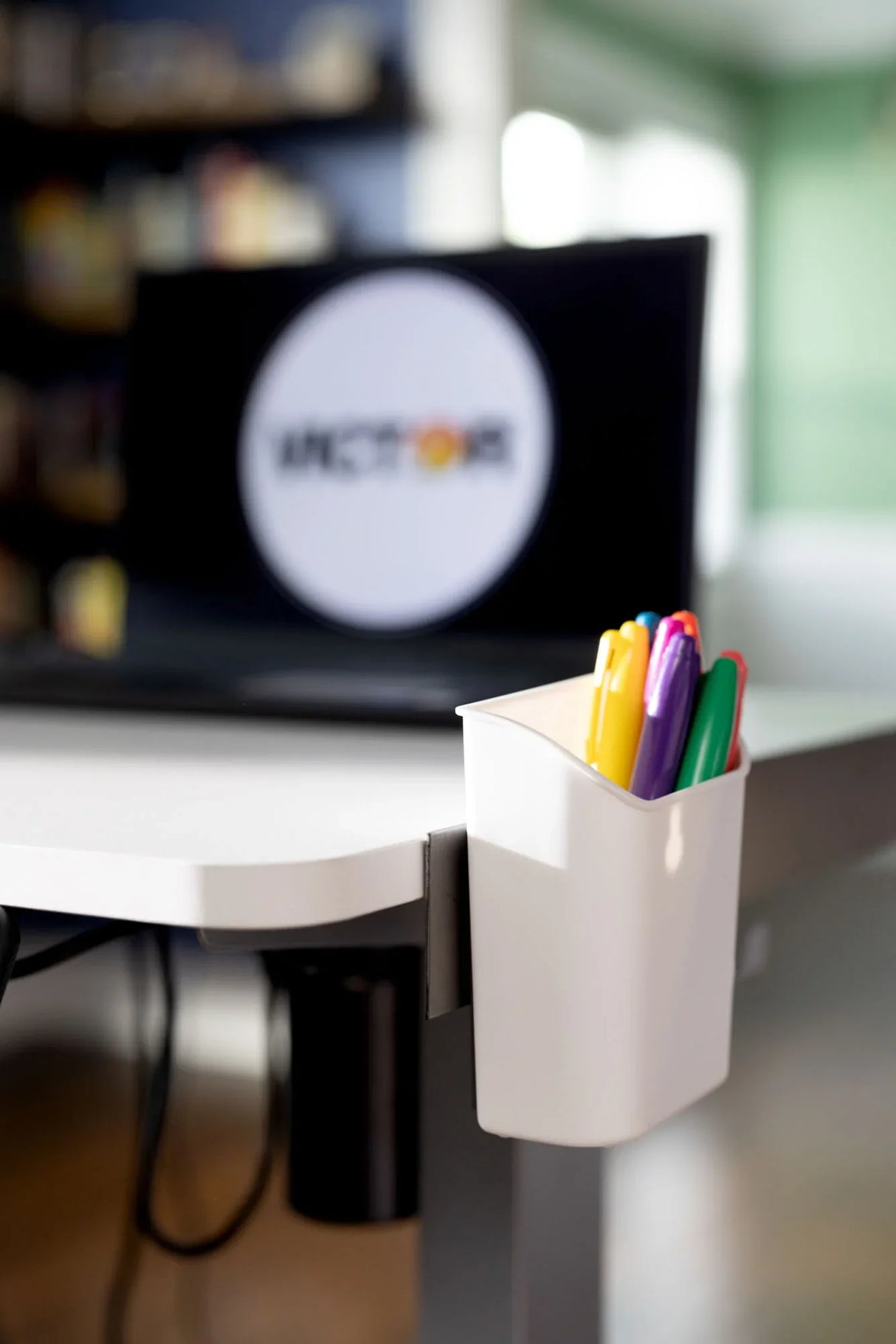 Desk clip-on pen holder with colorful pens, laptop blurred in background, modern office