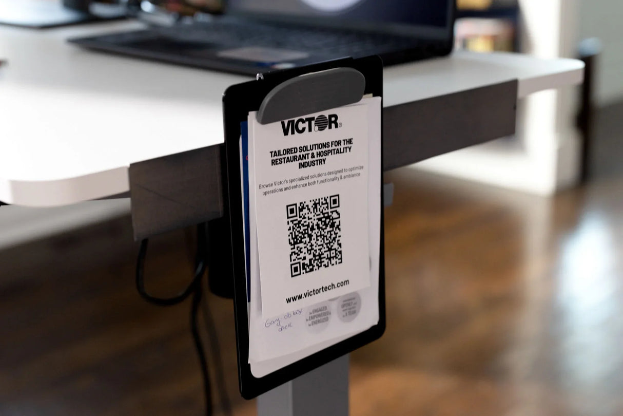 Document holder attached to a modern standing desk with a Victor info sheet and QR code in an office setting