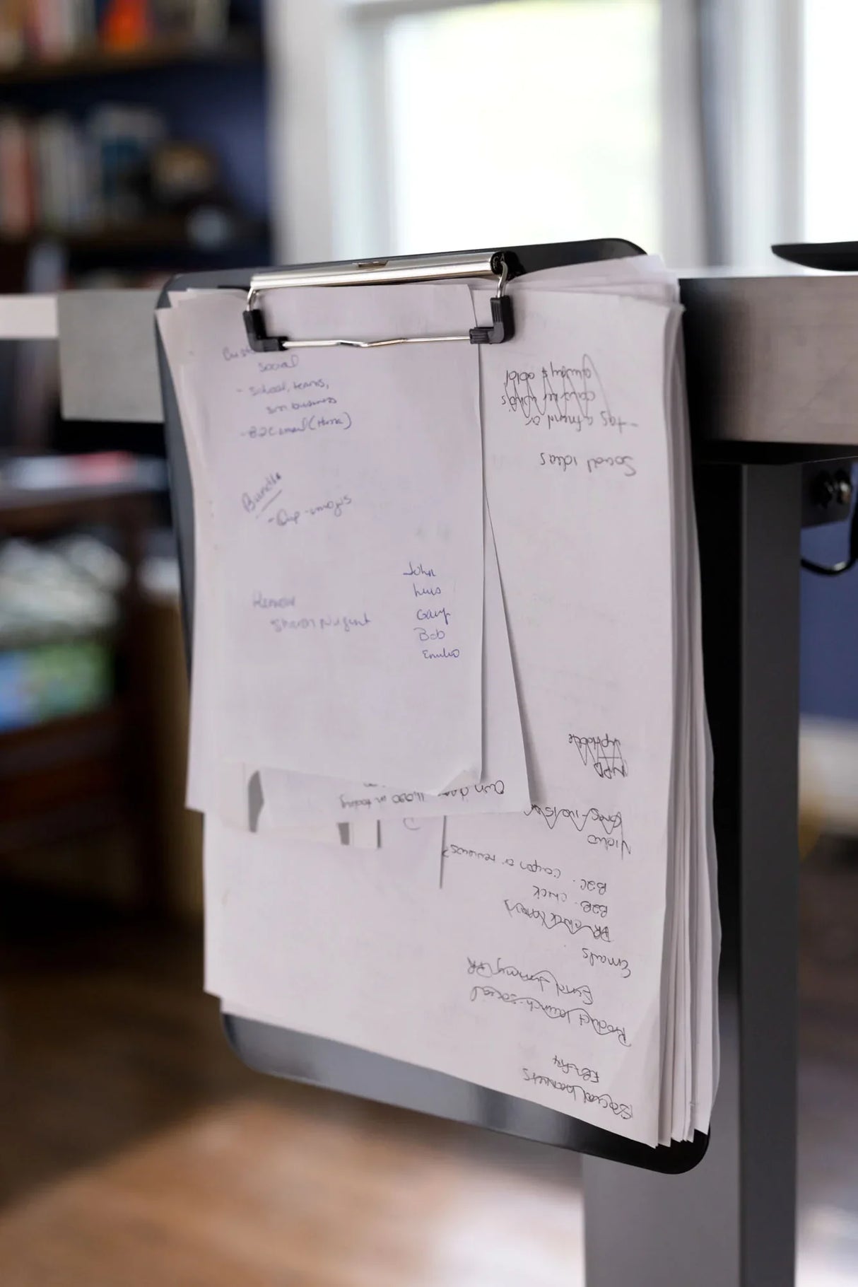 Clipboard holding handwritten notes attached to the side of a standing desk