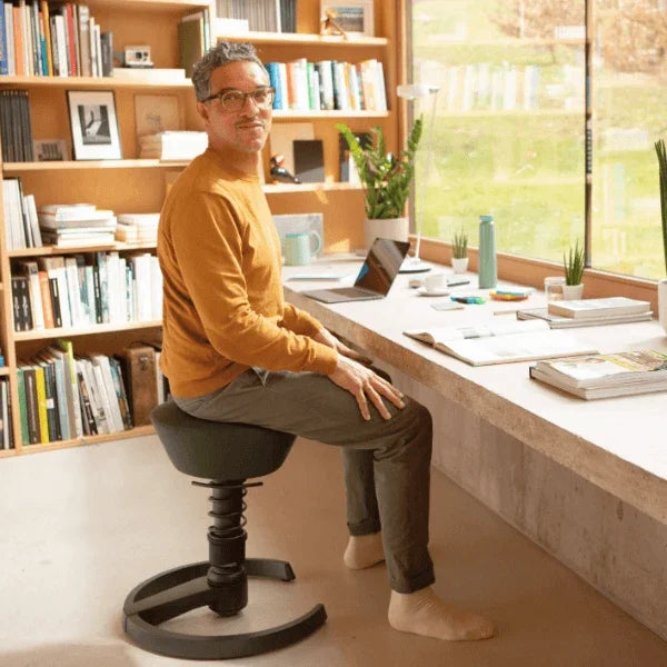 Man sitting on an Aeris Swopper ergonomic office stool at a desk in a home office.