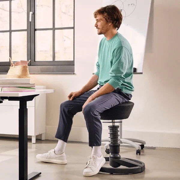 Man sitting on an Aeris Swopper Ergonomic Office Stool in a modern workspace.