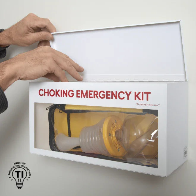 Hands opening wall-mounted choking emergency kit with clear window showing rescue device
