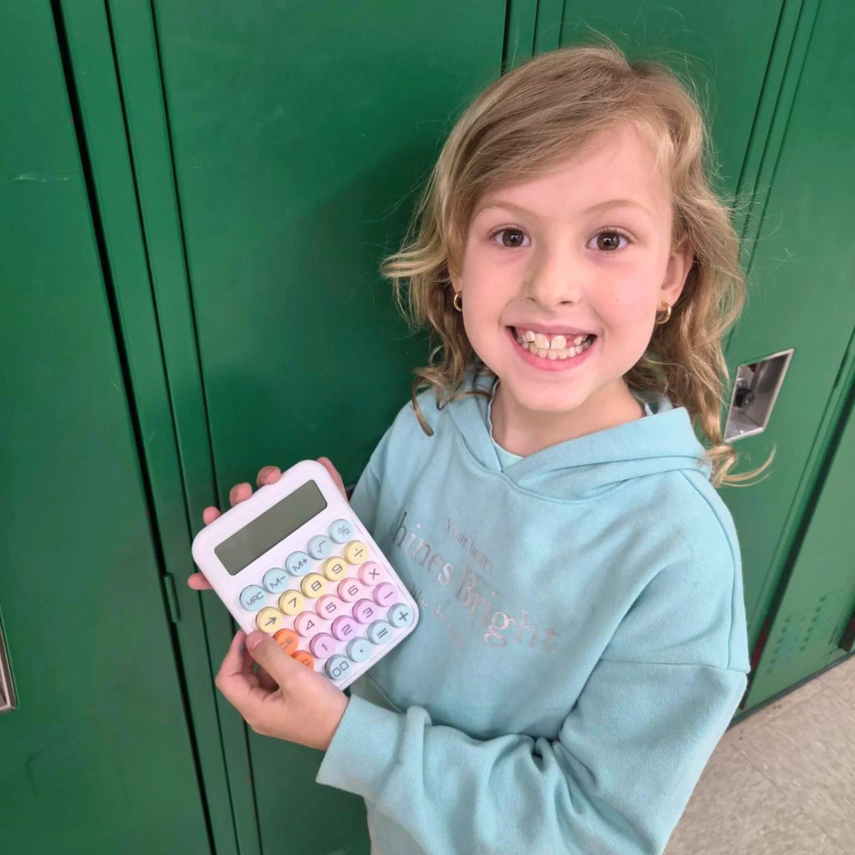 Child holding colorful calculator in front of green school lockers, perfect for school math and classroom use.