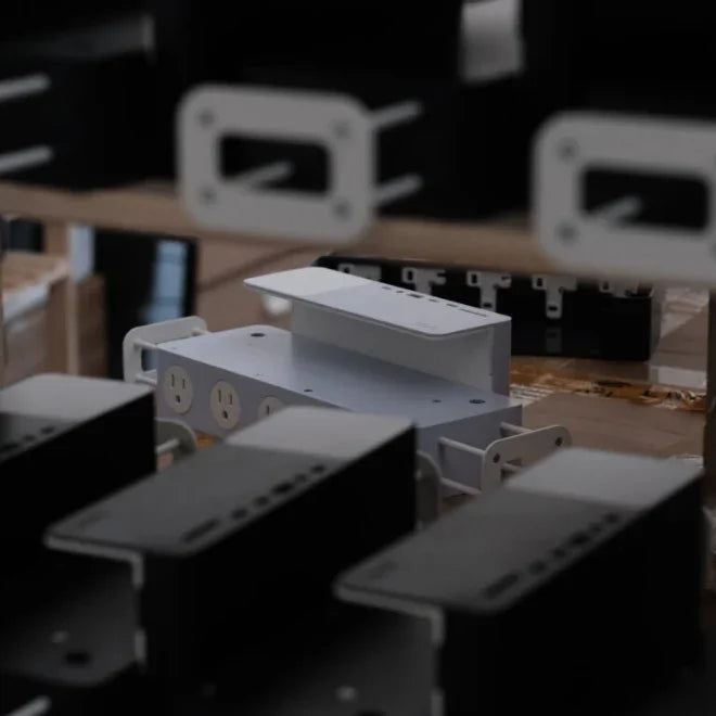 White metal desk organizer with built-in power outlets on a worktable among black organizers