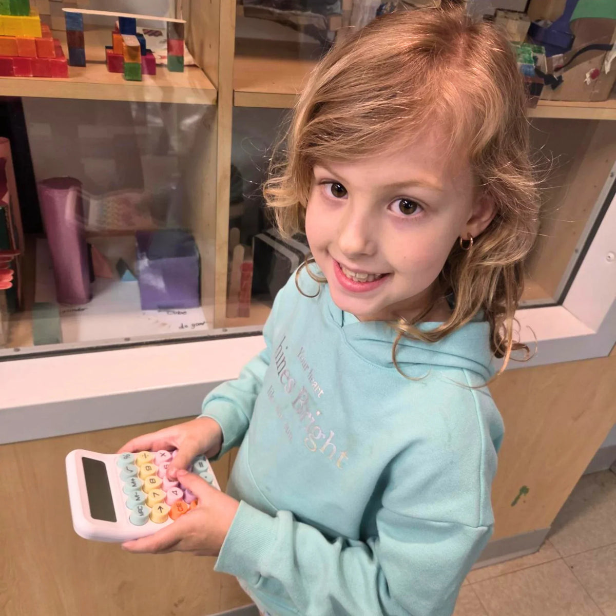 Child holding colorful calculator in classroom with educational toys