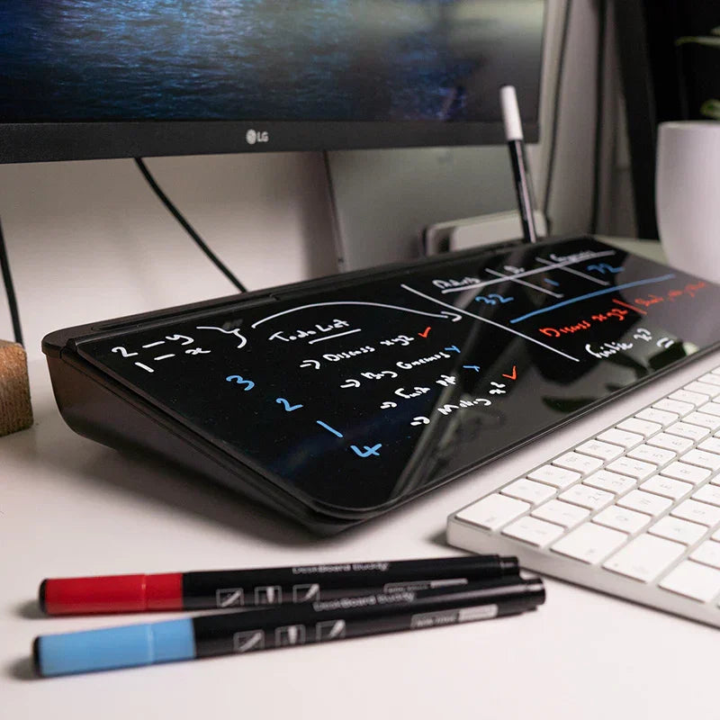 Glass desktop dry erase board with handwritten notes, keyboard, and markers in modern workspace
