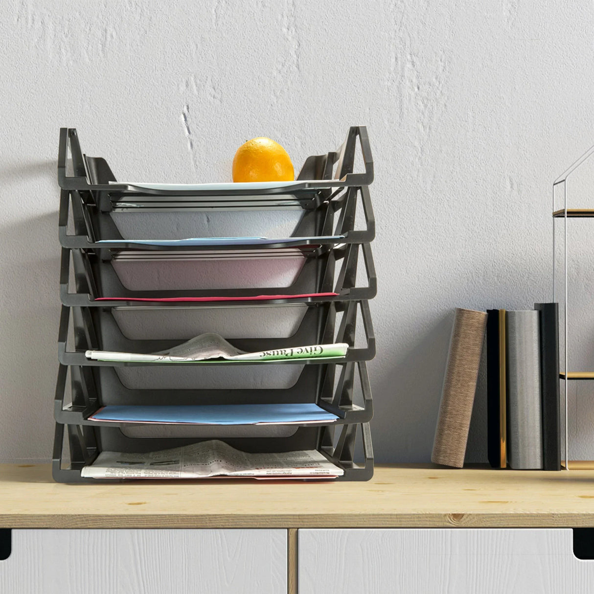 Black multi-tier document organizer with papers and an orange on top, placed on a wooden desk.