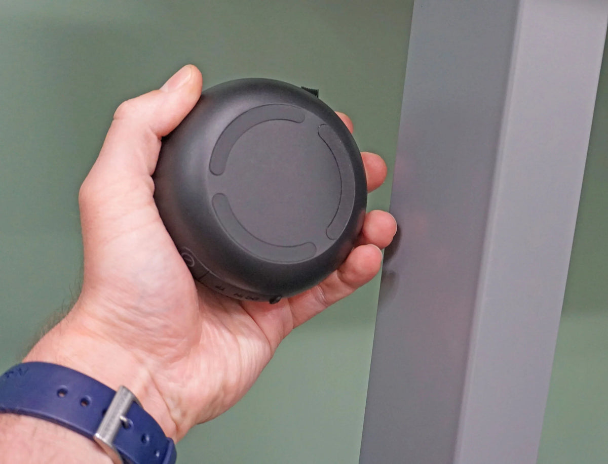 A hand holding a black Victor® MagnetPlus magnetic wireless speaker.