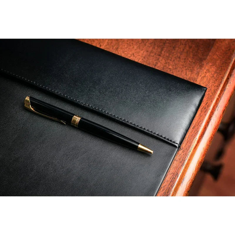 Black bonded leather desk pad with gold pen on wooden desk