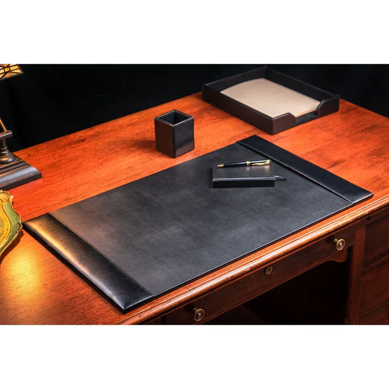 Black bonded leather desk pad on wooden desk with pen, organizer, and paper tray