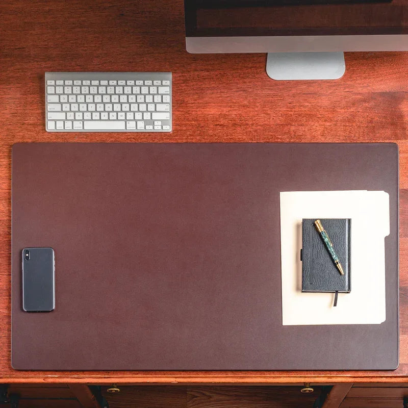Black chocolate brown leather desk mat on wooden desk with keyboard, phone, and notebook