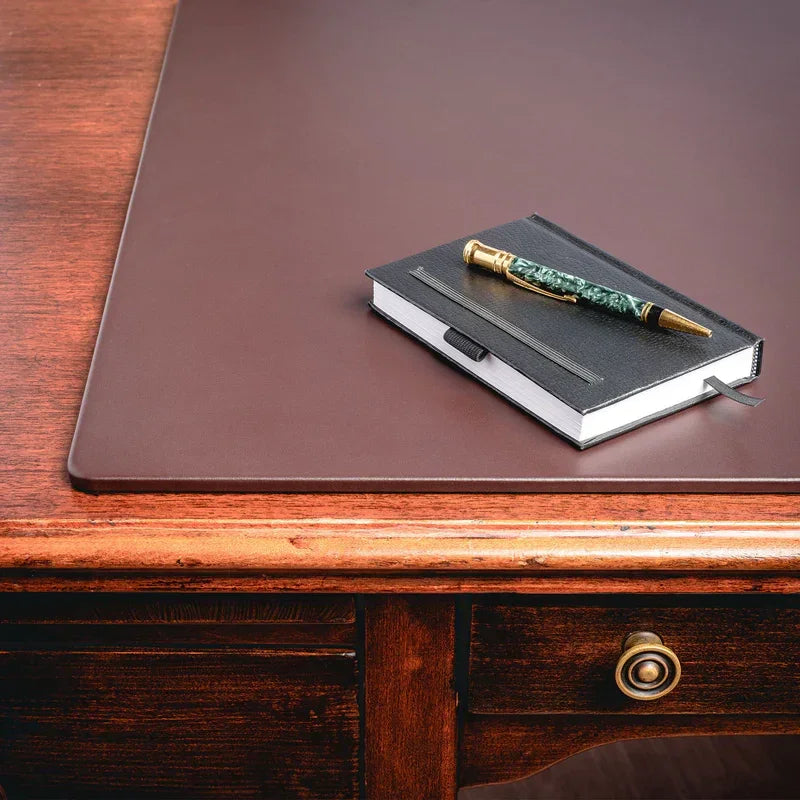 Brown leather desk mat on wooden desk with black notebook and pen