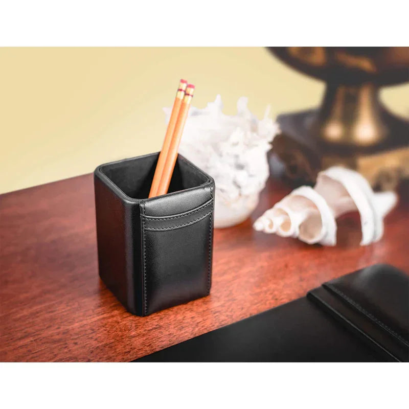 Black leather pencil holder with two pencils on a wood desk, seashells in background