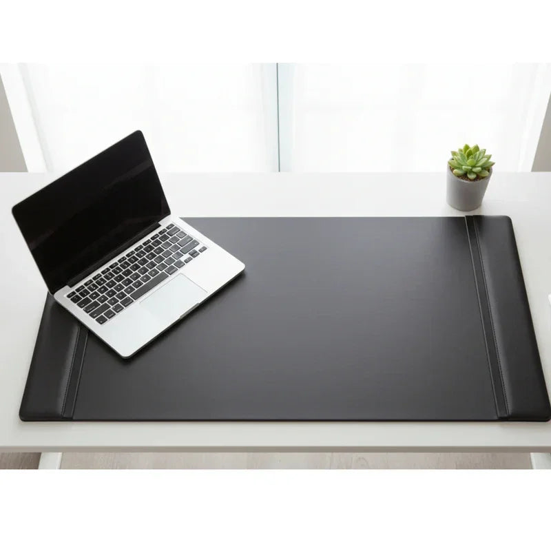 Black leather desk pad with side rails on white desk, laptop and small plant nearby