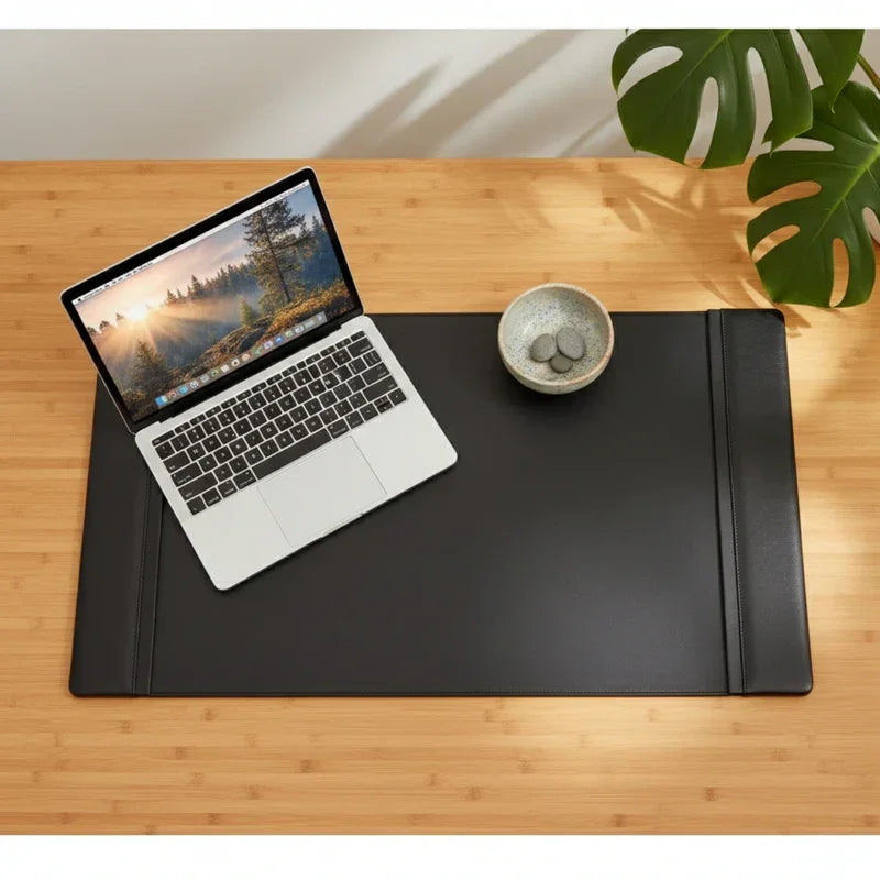 Black leather side rail desk pad on wood desk with laptop, bowl, and green plant