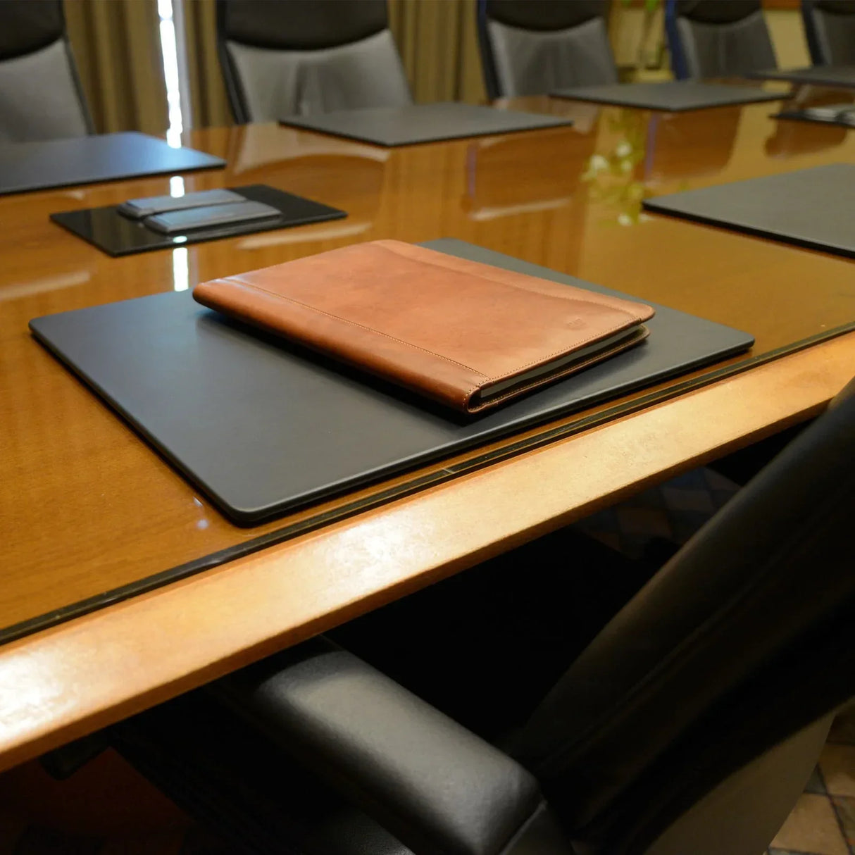Black leatherette 20 x 16 inch conference table pad on wooden meeting table with brown folder.