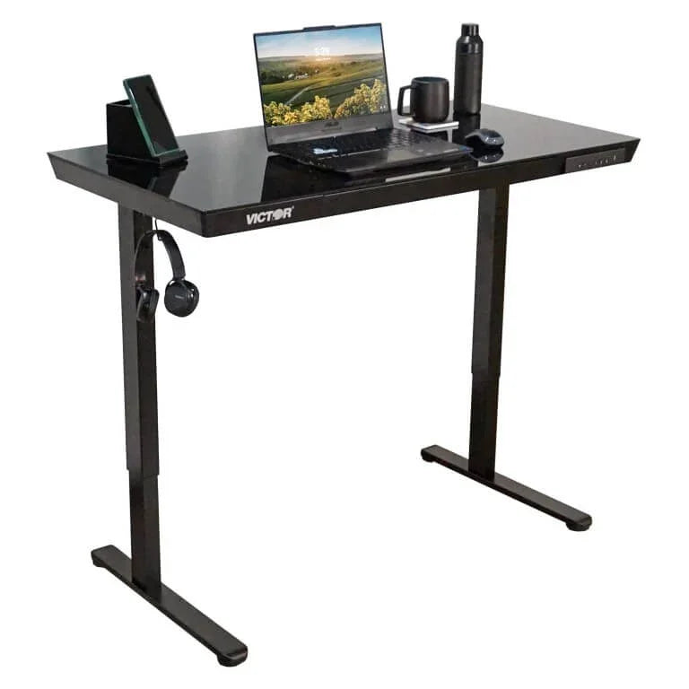 Victor® Electric Glass Topped Standing Desk with laptop, headphones, and accessories