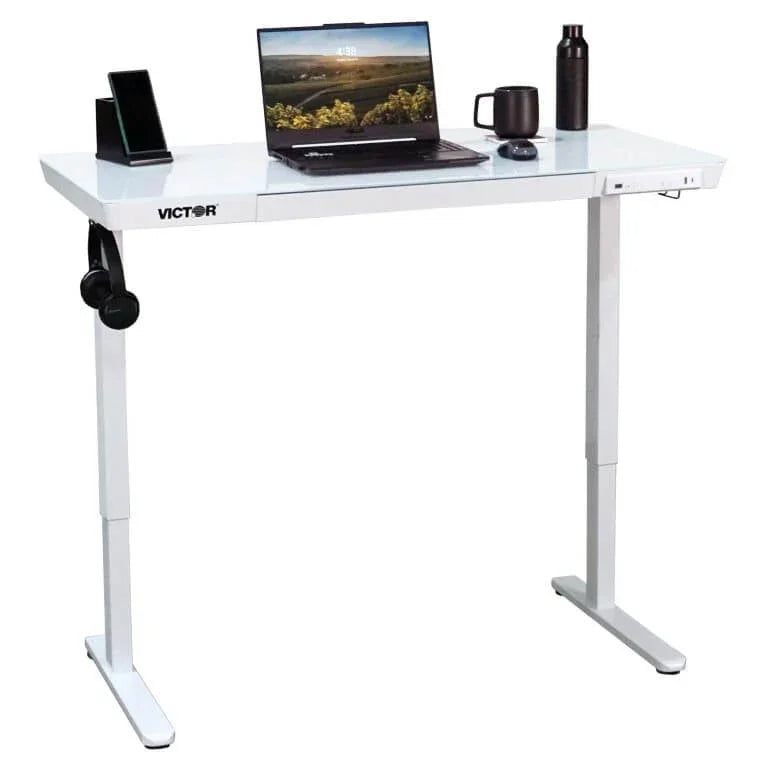 Victor® Electric Glass Topped Standing Desk in white with laptop, headphones, and accessories