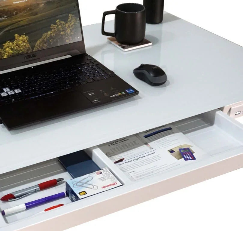 Victor® electric glass topped standing desk with an open drawer containing office supplies.