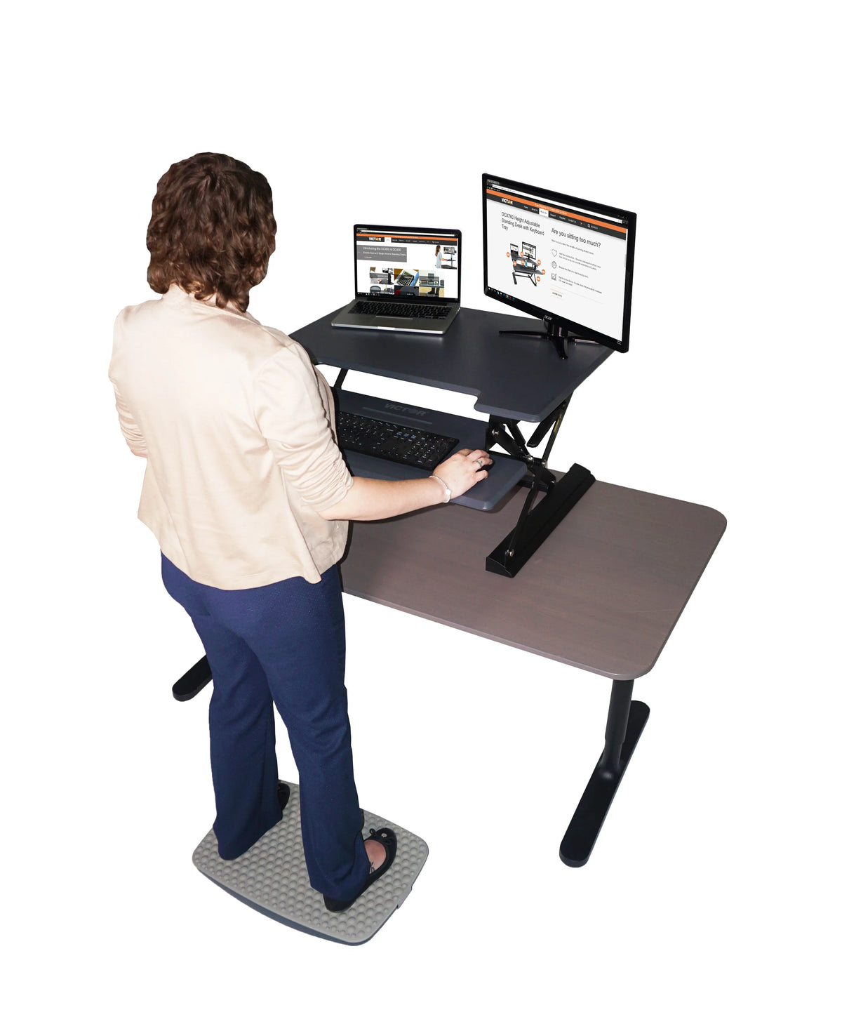 Woman using a Victor standing desk converter while standing on a Steppie Balance Board.