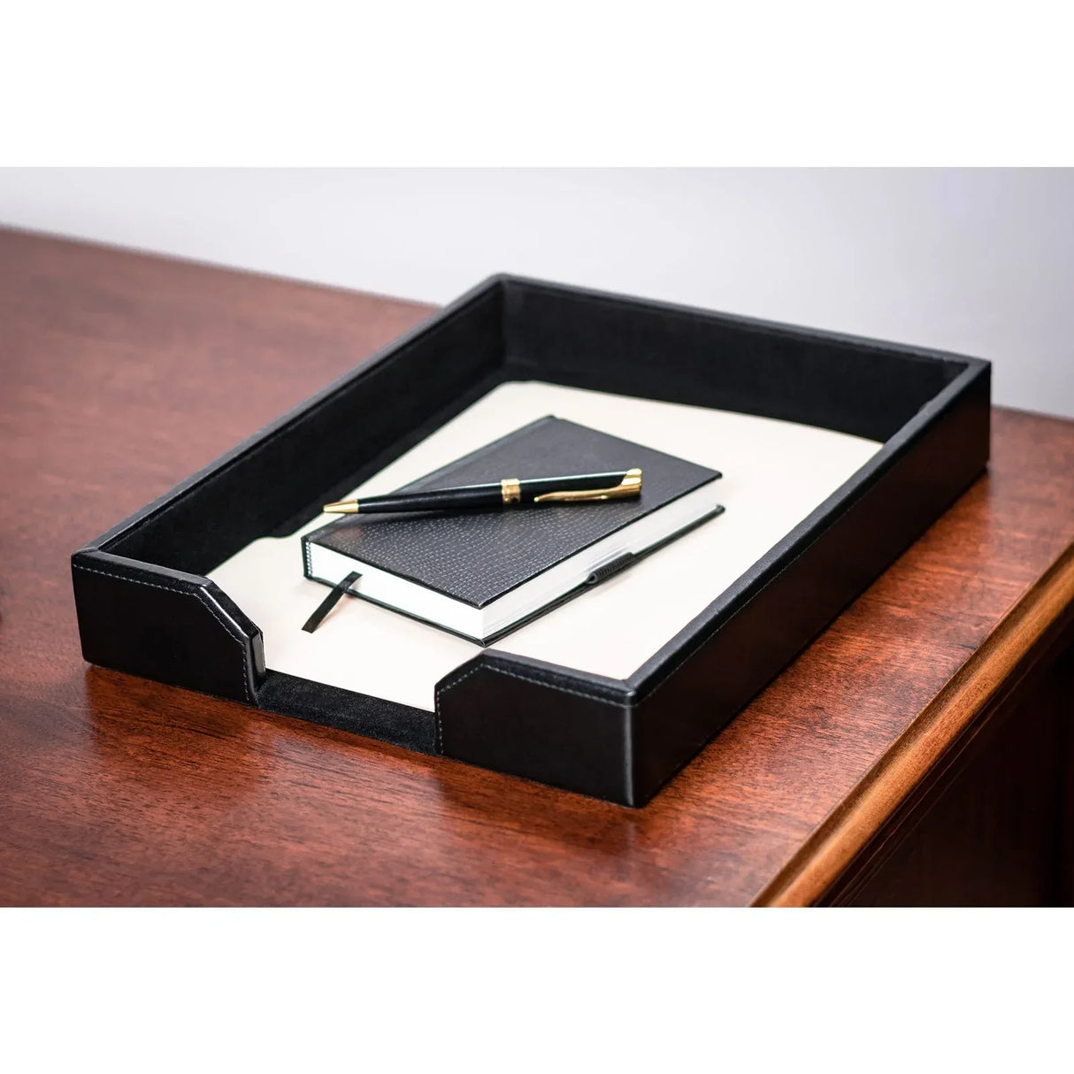 Black leather letter tray on wooden desk with notebook and pen, office organizer accessory