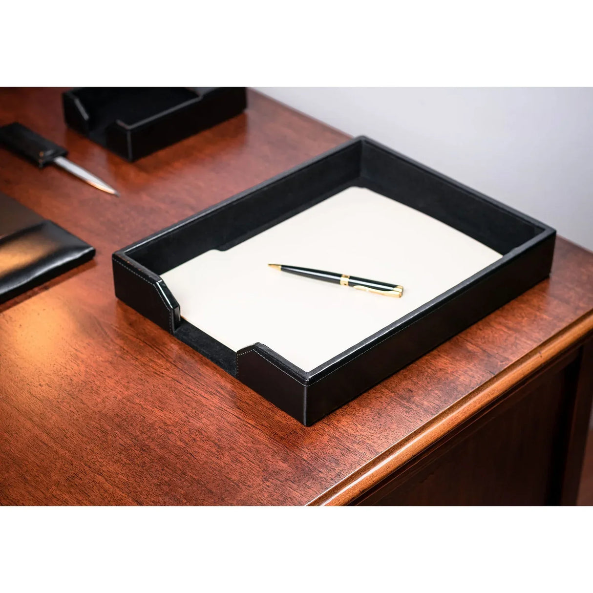 Black leather letter tray with white paper and pen on wooden office desk