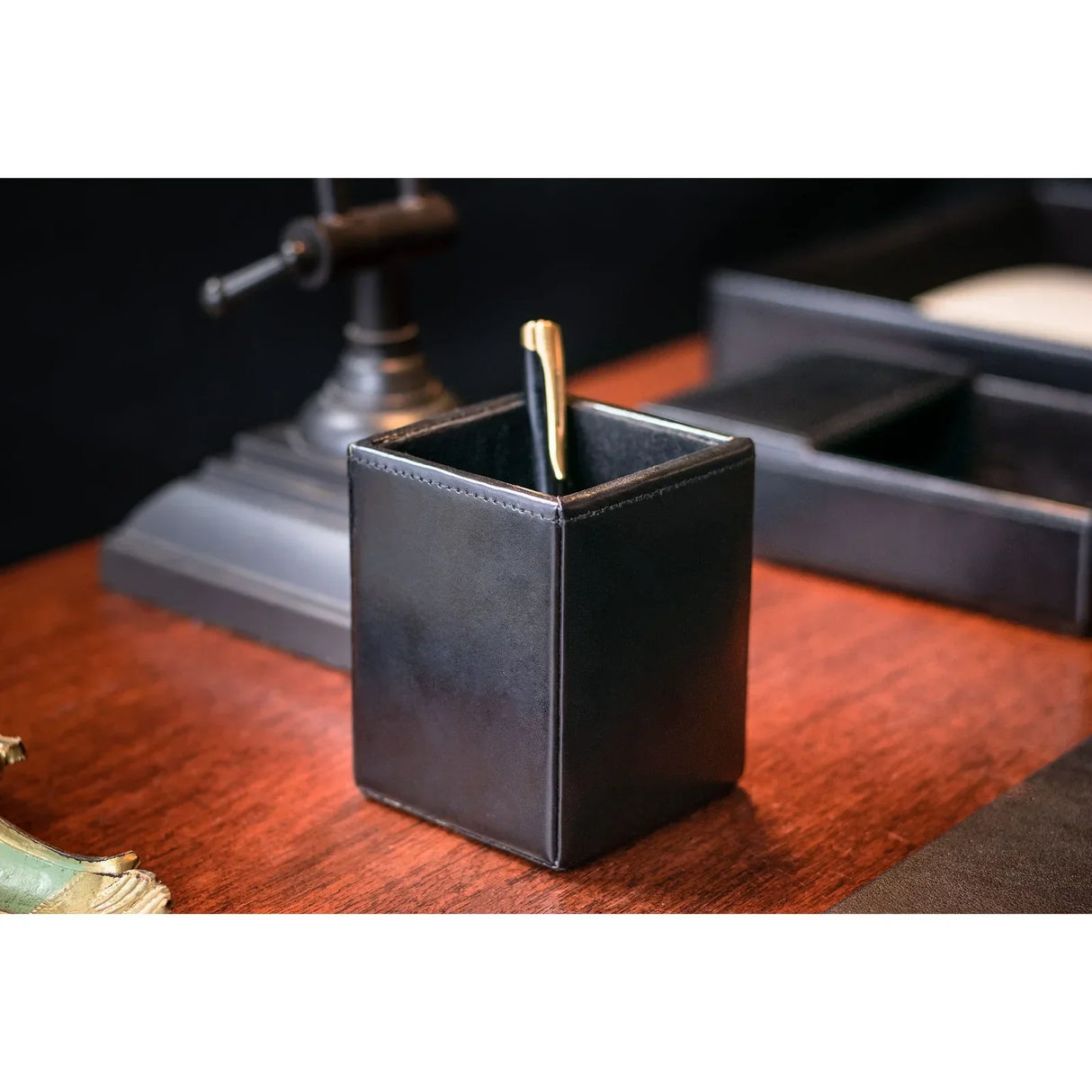Black leather pencil cup organizer holding a pen on a wooden desk