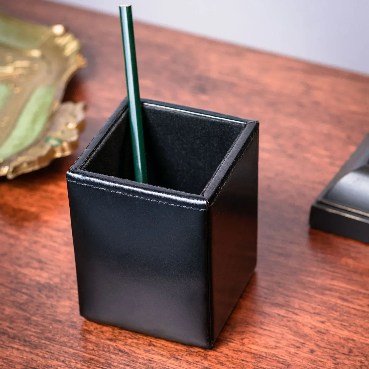 Black leather pencil cup organizer on wooden desk with a green pencil inside
