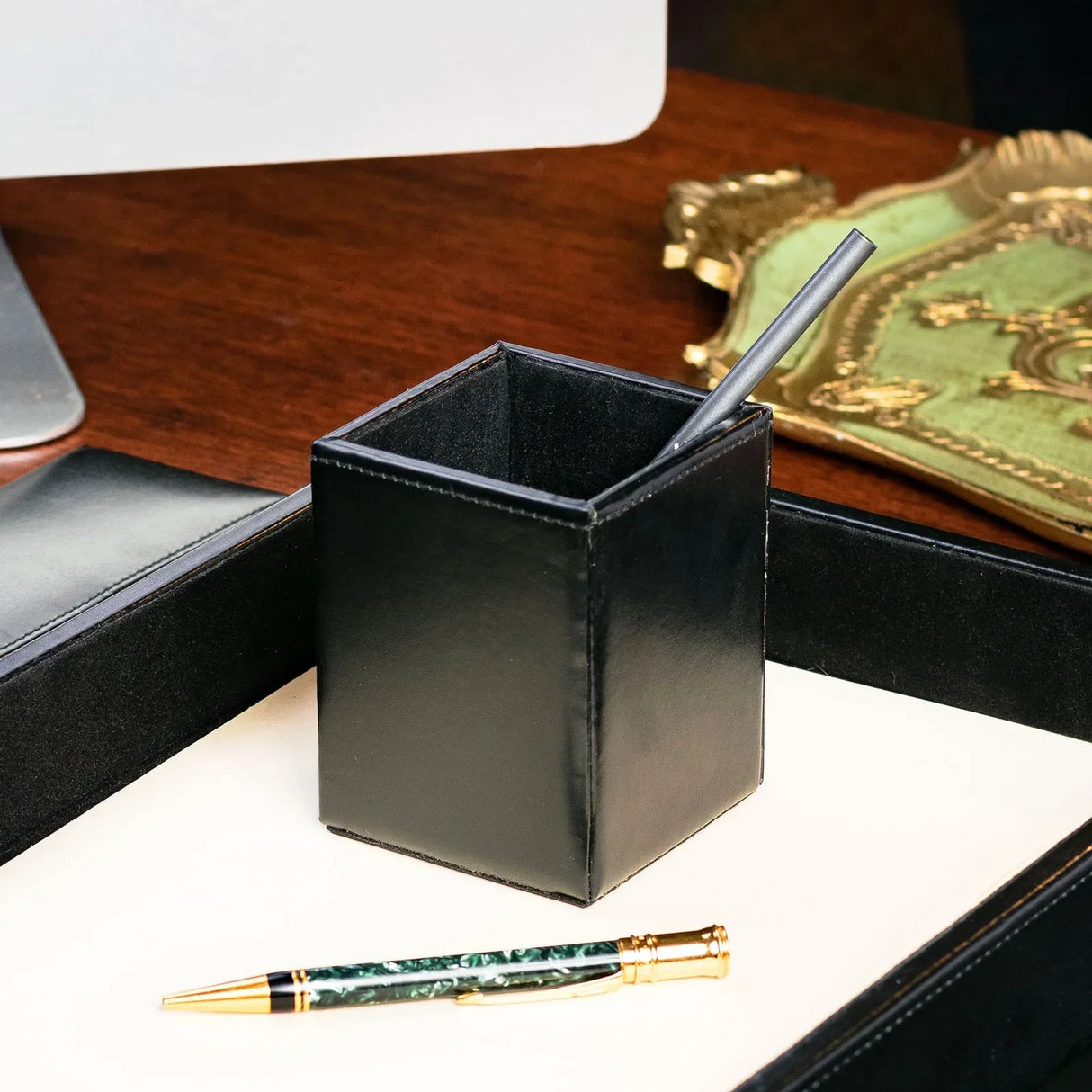 Black leather pencil cup on an office desk with a pen and tray, workspace organizer