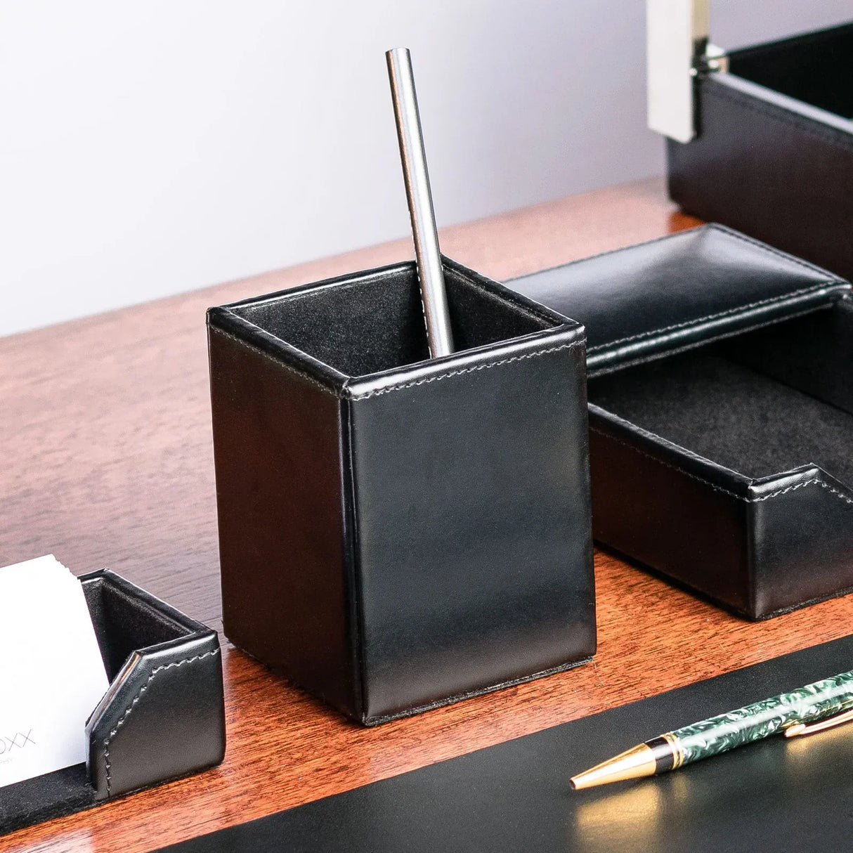 Black bonded leather pencil cup on wood desk with metal pen and office organizers