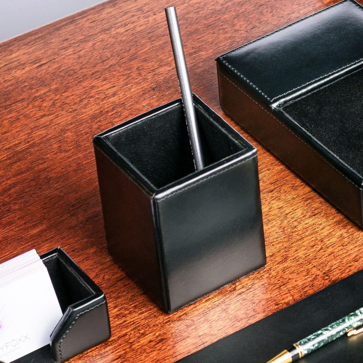 Black leather pencil cup organizer on wooden desk with office accessories
