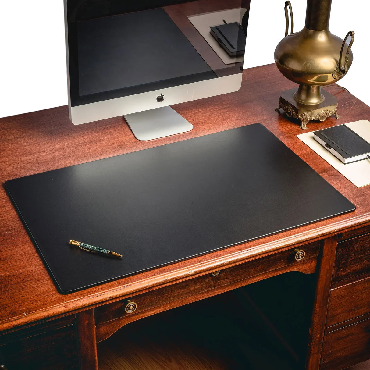 Black leather desk mat on a wooden office desk with computer, lamp, and pen