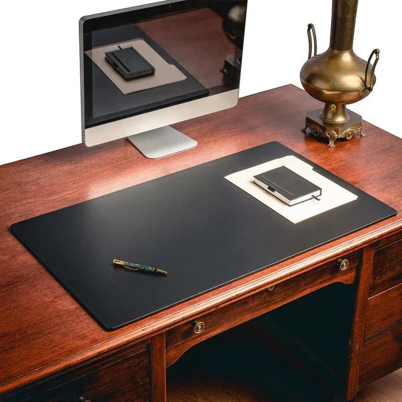 Large black leather desk mat on wooden desk with computer, lamp, notebook, and pen