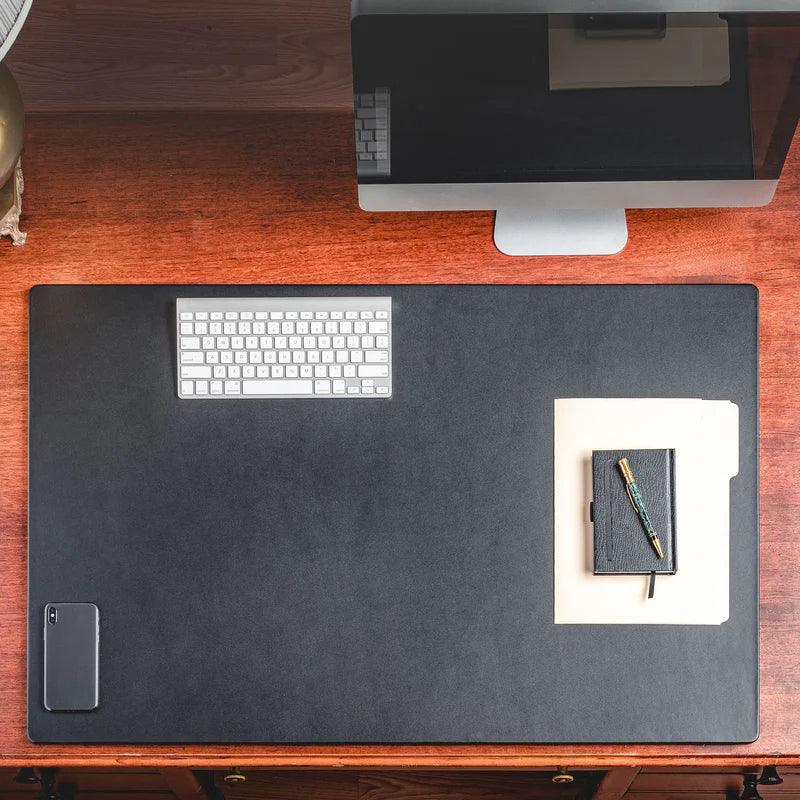Black leather desk mat on wood desk with computer, keyboard, phone, folder, notebook, and pen