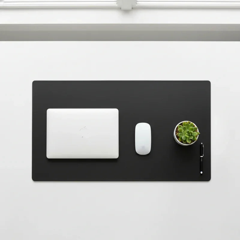 Black leather desk mat with laptop, wireless mouse, pen, and small potted plant on white desk