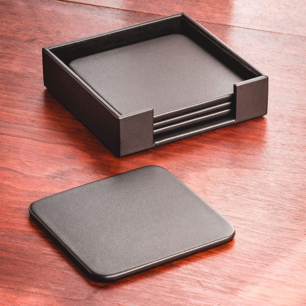 Black leather square coaster set with holder on wooden desk