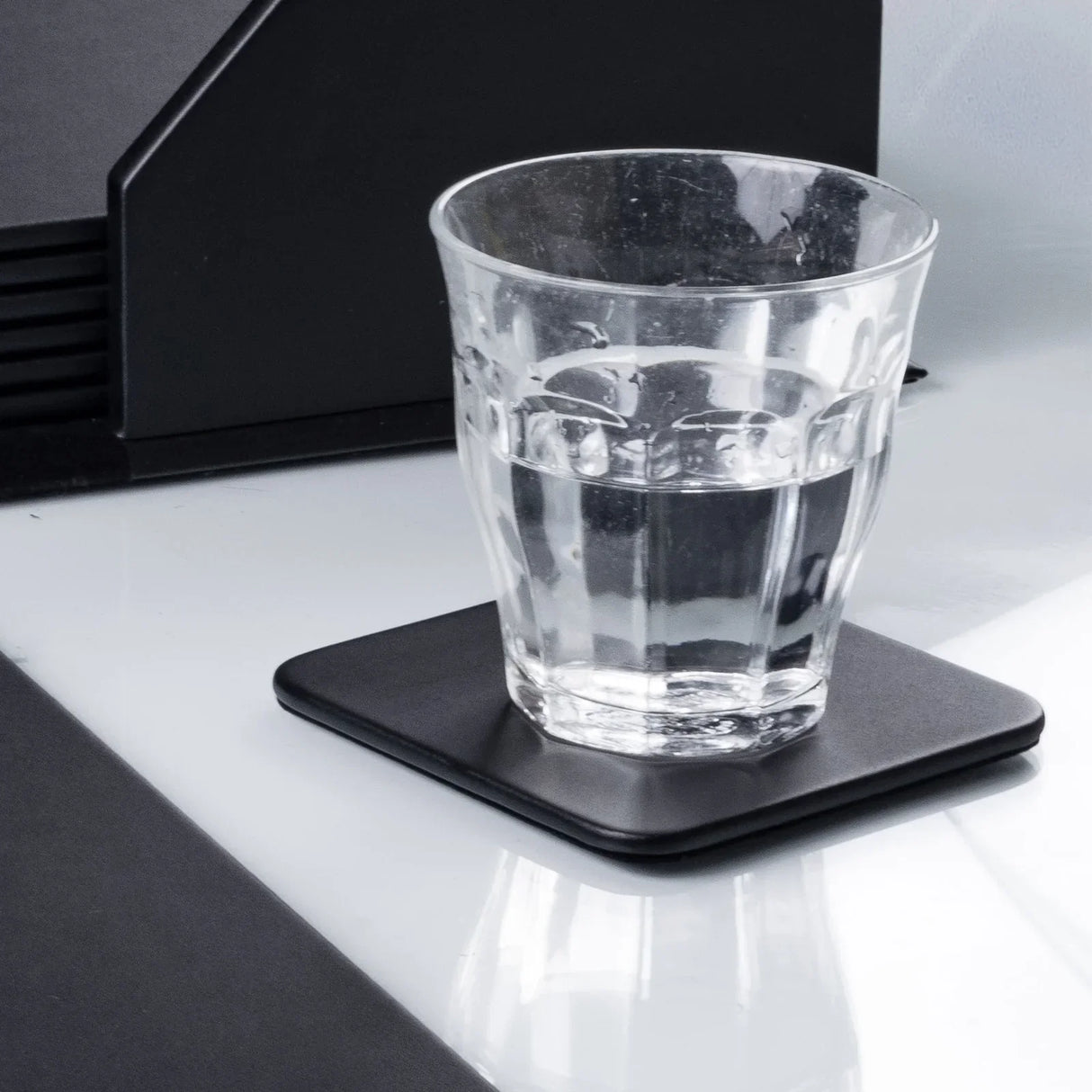 Glass of water on a black leatherette square coaster on office desk