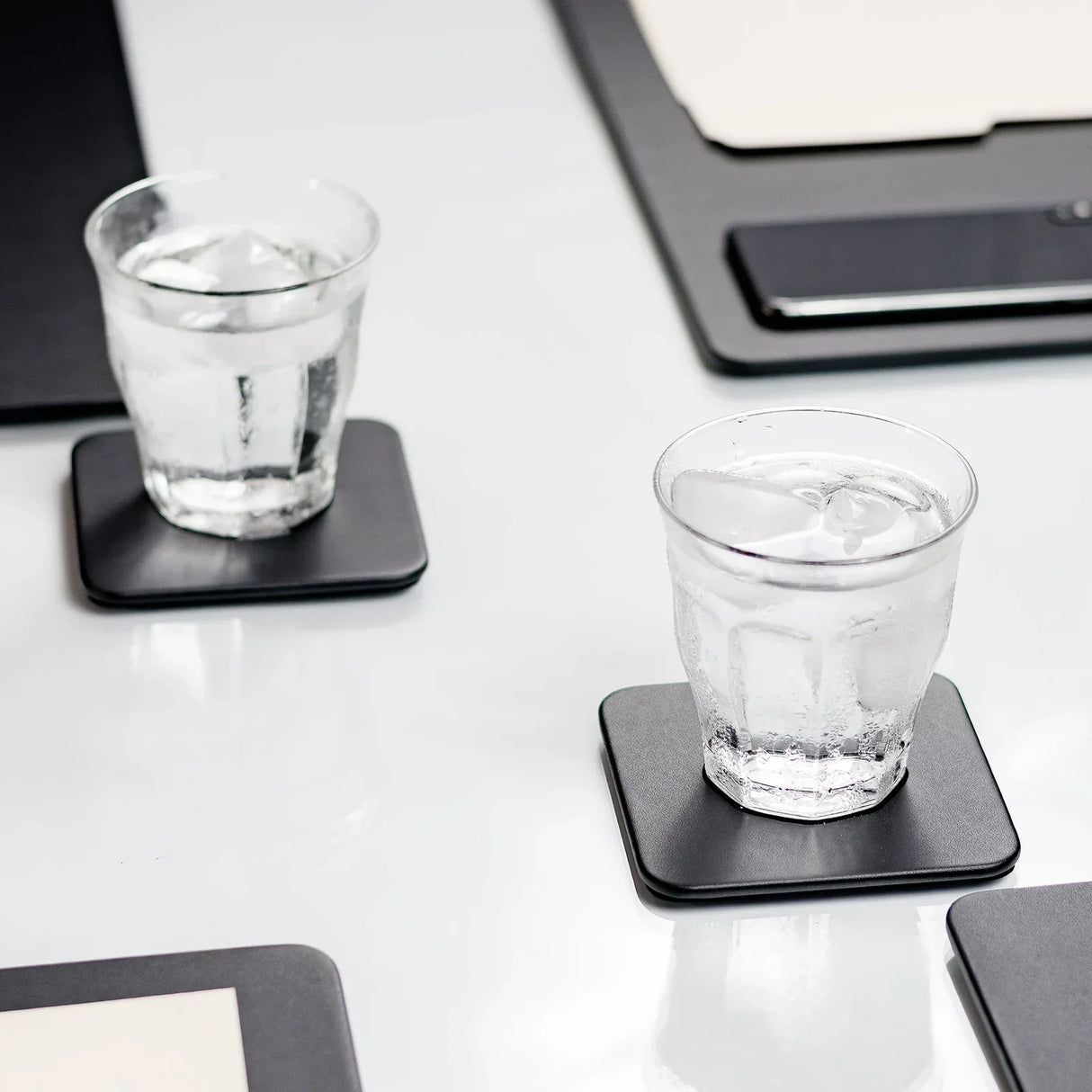 Black leatherette square coasters holding glasses of ice water on a modern office desk