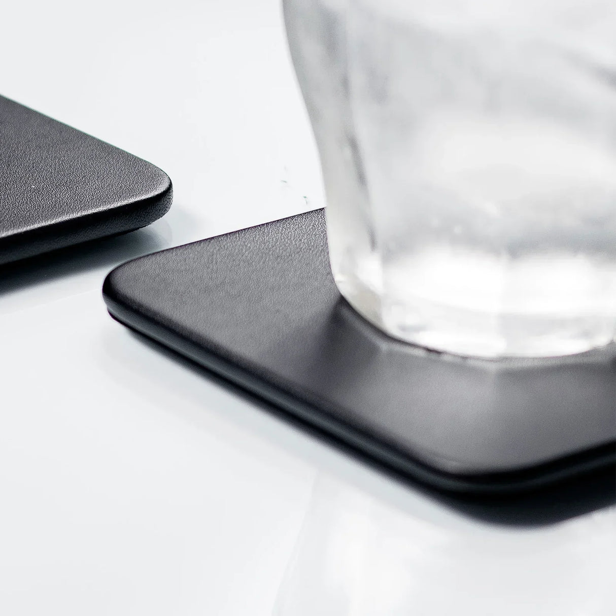 Black square leatherette coaster with glass on modern workspace surface