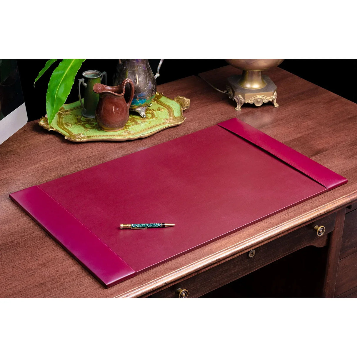 Burgundy leather desk pad on wooden office desk with pen and decorative tray