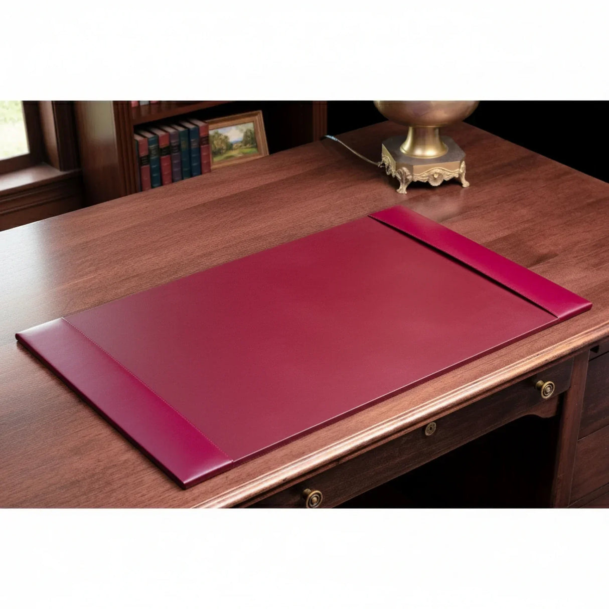 Burgundy bonded leather desk pad on wooden office desk with books and lamp in background