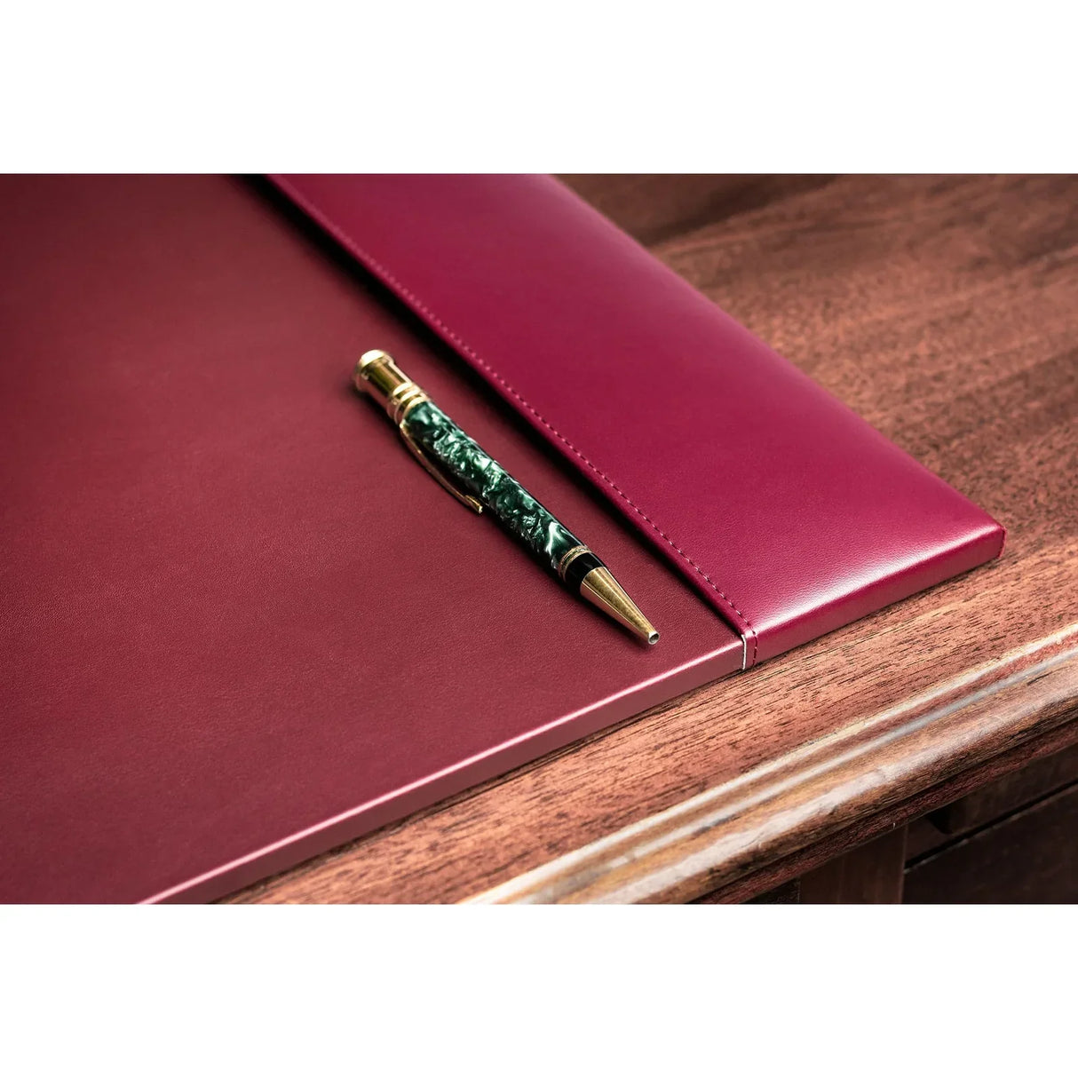 Burgundy leather desk pad with a gold and green pen on a wooden desk