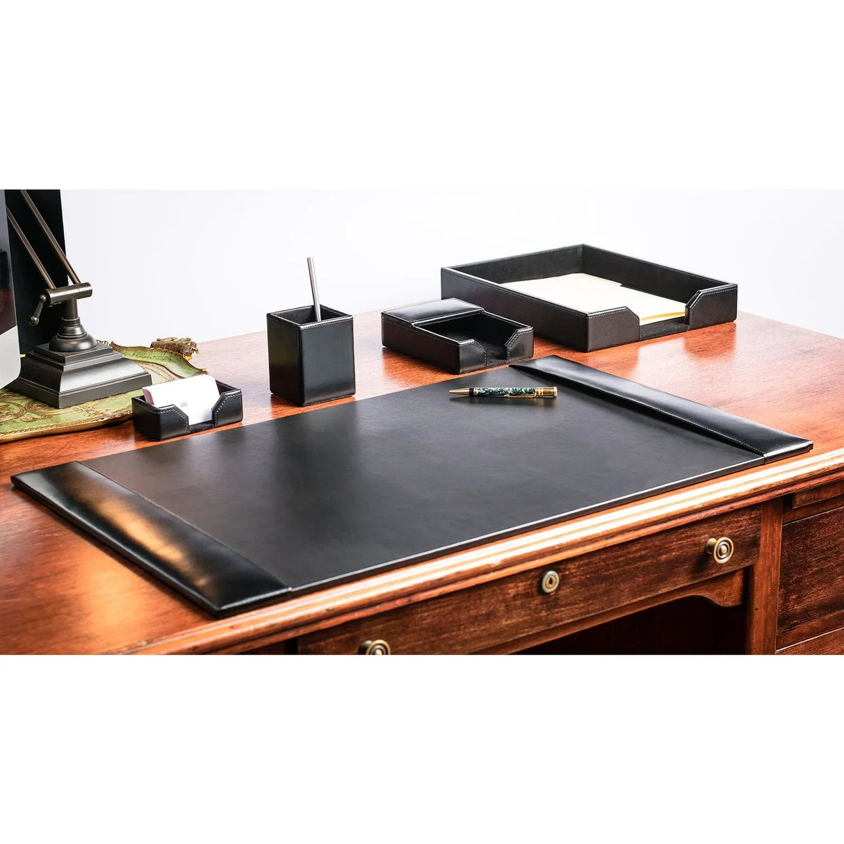 Black leather desk organizer set with mat, trays, and pen holder on wooden office desk