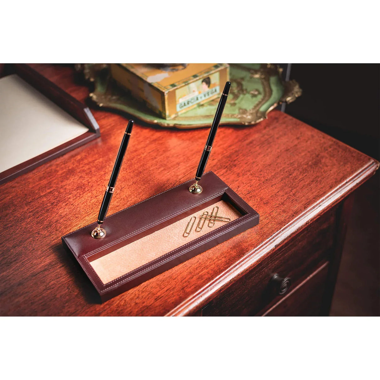 Brown leather desk organizer with two black pens and paper clips on a wooden office desk.