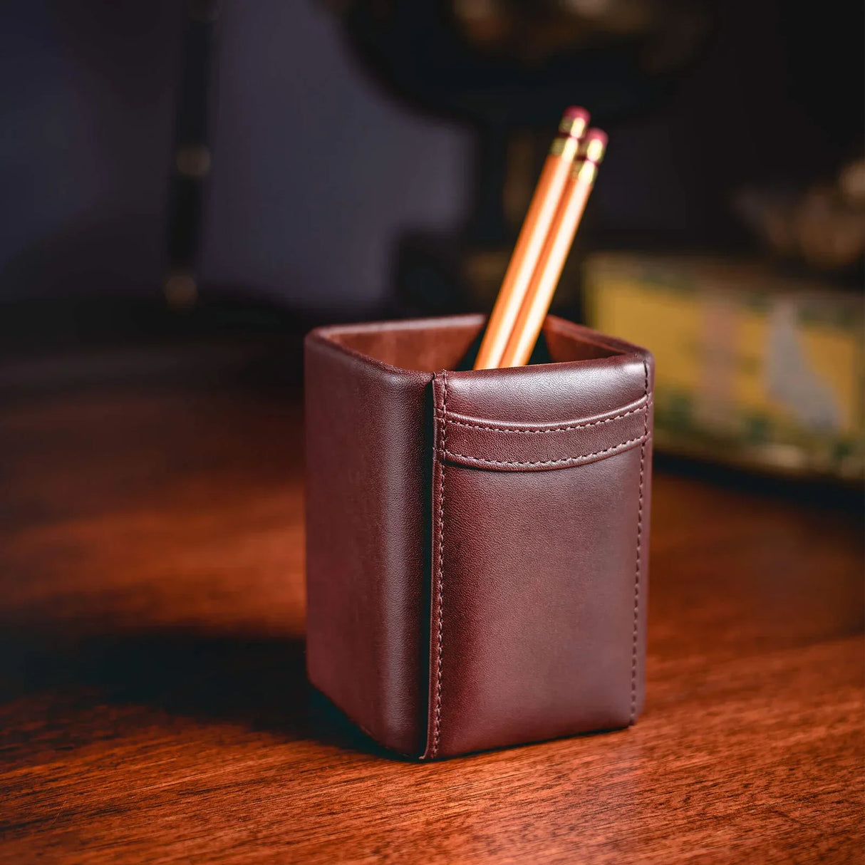 Brown leather pencil holder with two pencils on a wooden desk