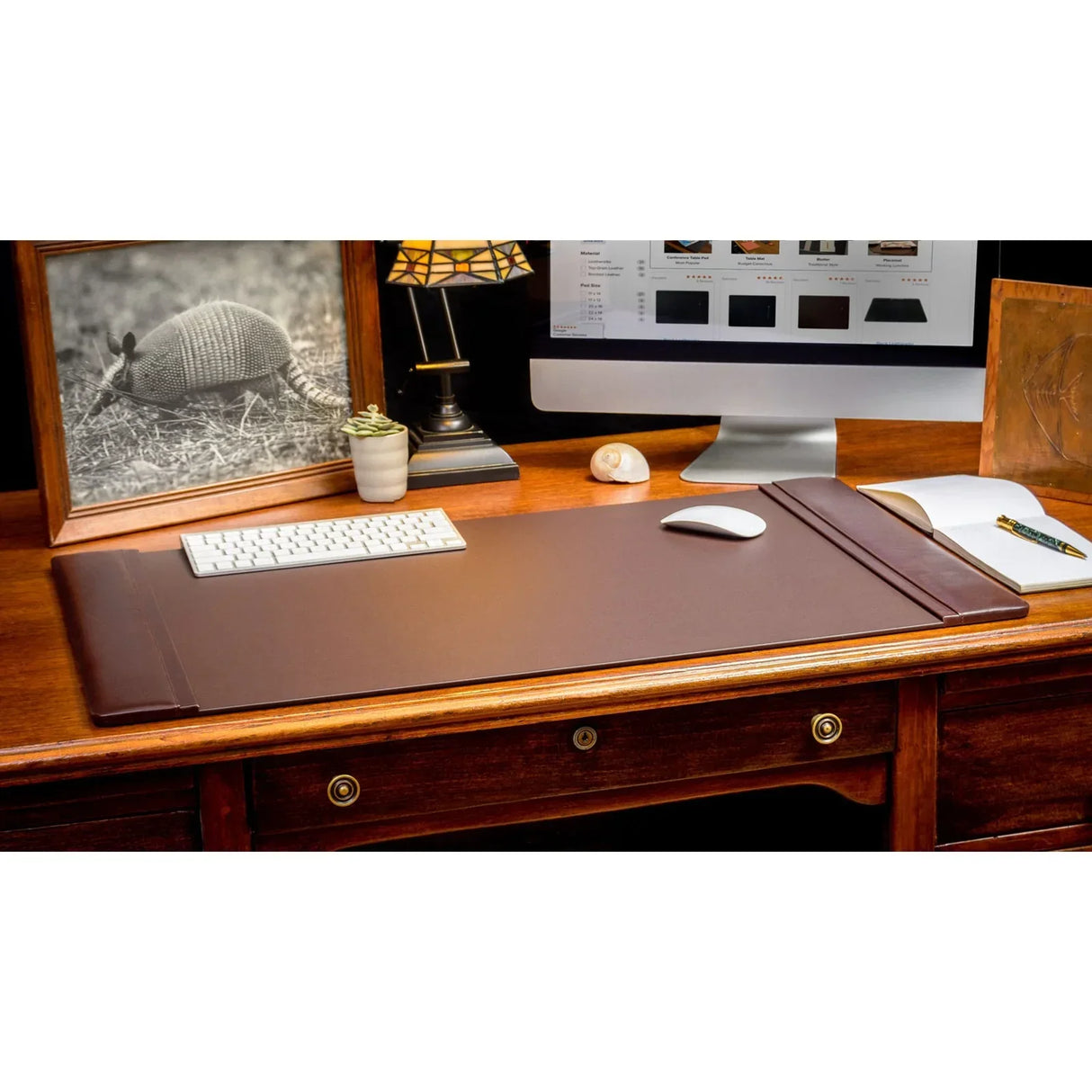Chocolate brown leather desk pad on wooden desk with computer, keyboard, and lamp
