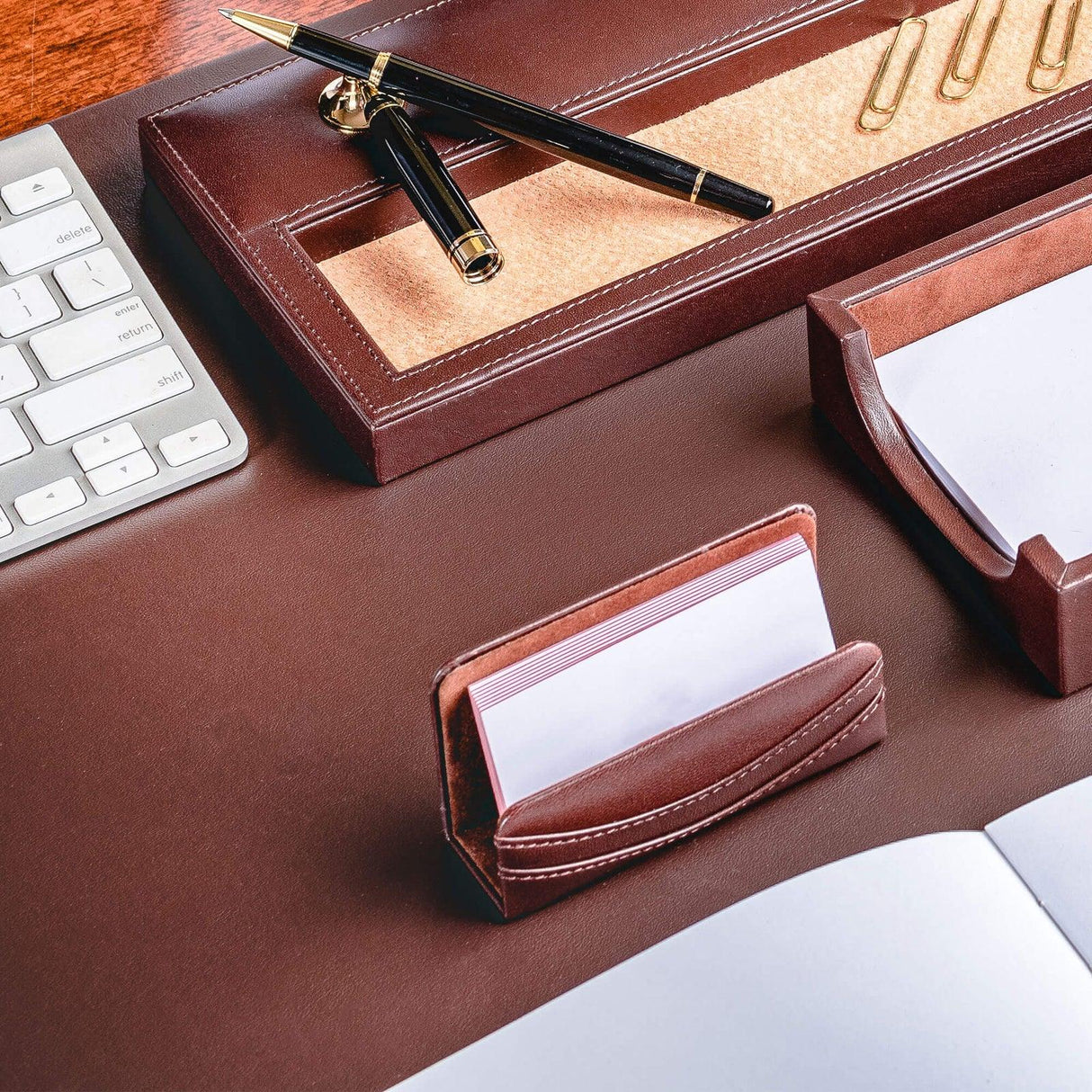 Chocolate brown leather desk set with card holder, paper tray, pen holder, and keyboard on a desk