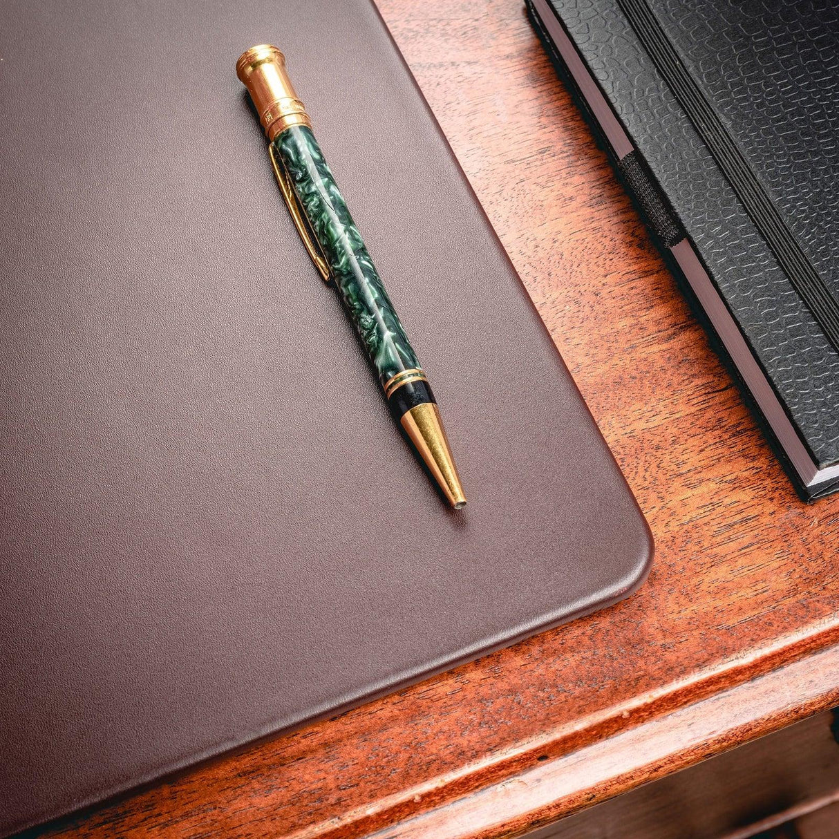 Chocolate brown leather desk mat on wooden desk with pen and black notebook