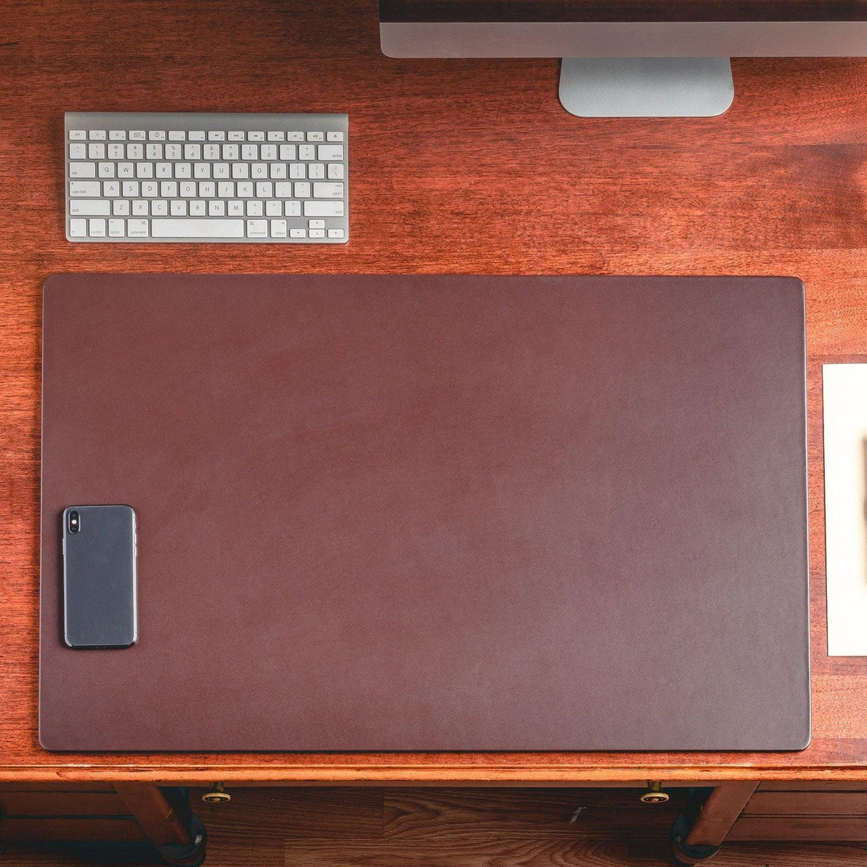 Chocolate brown leather desk mat on wooden desk with phone, keyboard, and monitor